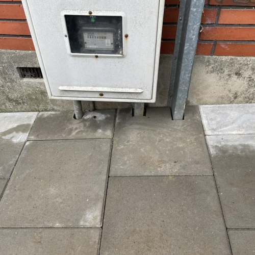 Anlægsarbejde ved bolig med nylagt flisebelægning og maskiner i gårdrummet.