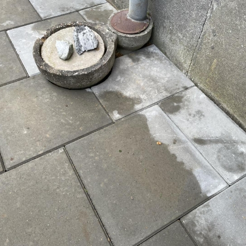 Lang flisegang langs husfacade med store mørke belægningssten og afrettet jord ved siden af.