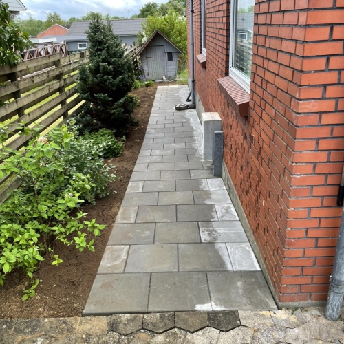 Nyanlagt terrasse i mørke fliser med trin og åbent haveareal omkring huset.