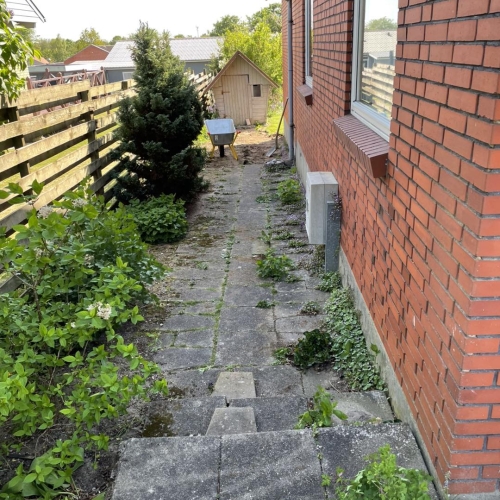 Stor fliseterrasse og gangsti rundt om bolig med jord klar til græs og beplantning.