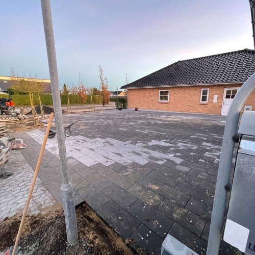 Stor flisebelægning ved bolig under færdiggørelse med støv og rester efter anlægsarbejde.