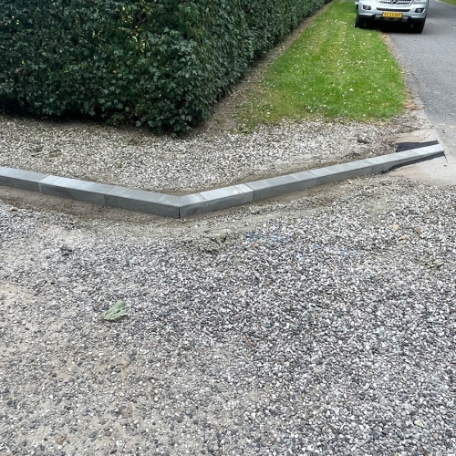 Detalje af hjørne med kantsten mellem vej, grus og grøn rabat.