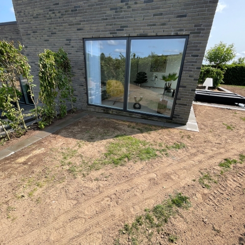 Terrasseområde ved moderne bolig med ny belægning og jord klar til beplantning.